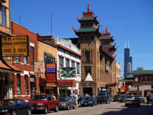 Chicago's Chinatown sits background of the image. A busy street is lined with cars and tall buildings with Chinese architecture sit above them.