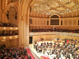 The interior of a grand performing arts center is photographed with the Chicago Symphony Orchestra seated on its stage.