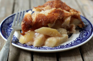 A slice of apple pie sits on a decadent plate with a fork.