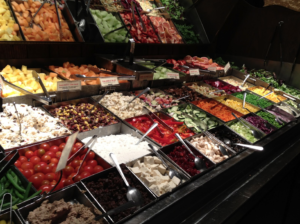 A salad bar holds a dozen or more containers of containers with a variety of salad toppings on it.